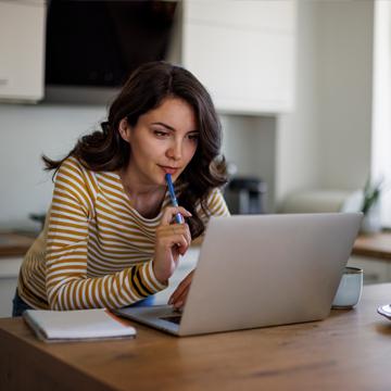 woman looking pensively at laptop screen and holding a pencil